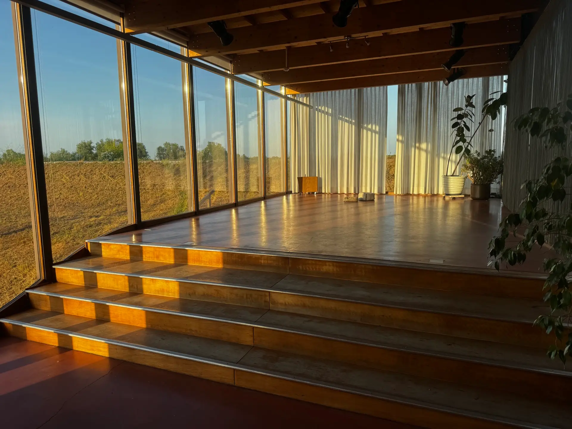 De kas van het Veerhuis: lichte zaal met lange houten tafel, uitzicht op de tuin en de Waal